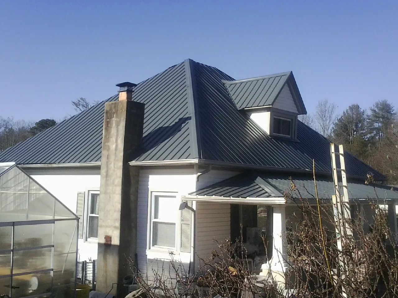 Dark blue standing seam metal roof on a white farmhouse with dormer — Slate & Tile Roof Repair by Roofing Brothers in Berkey