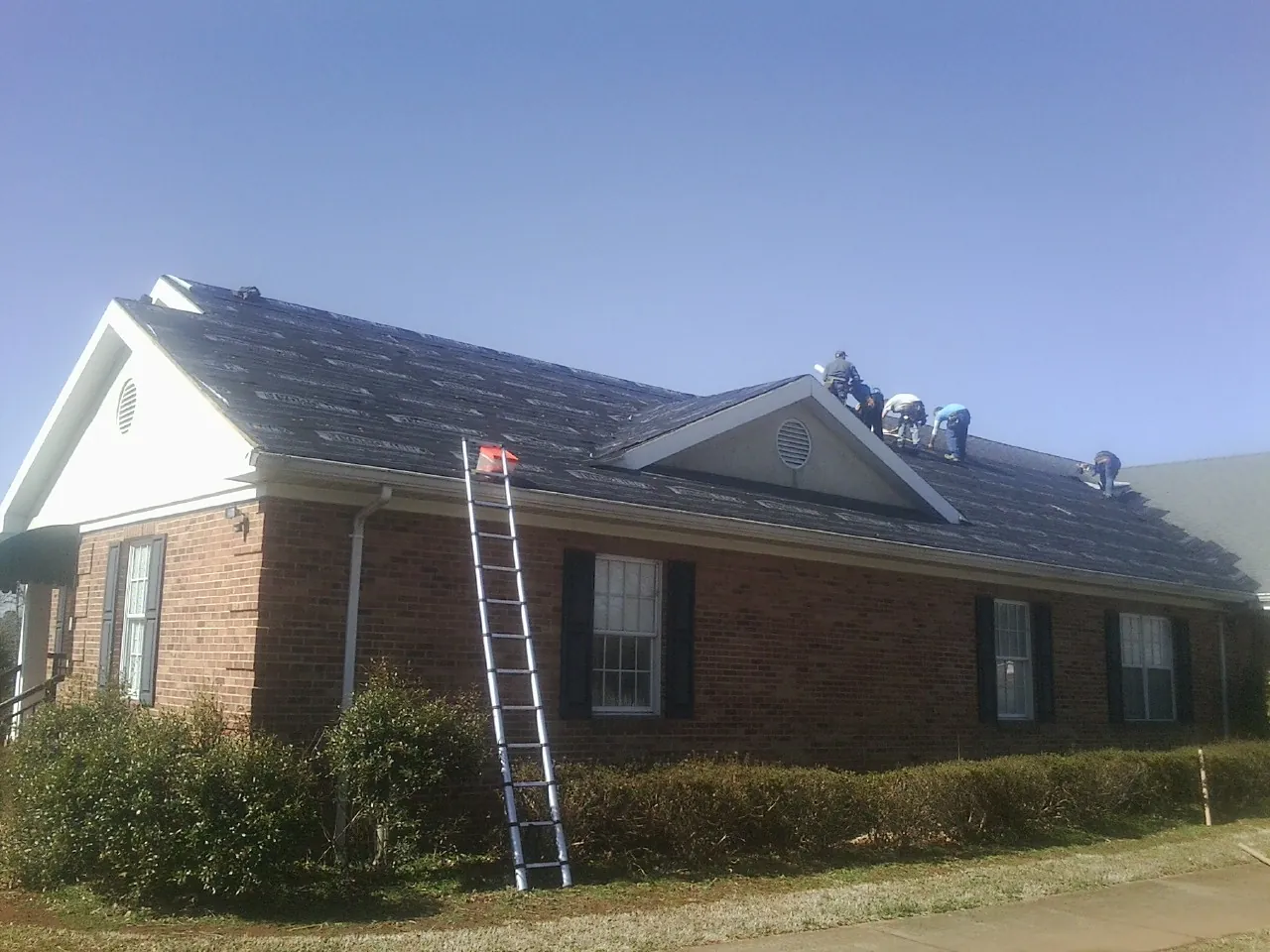 Crew tearing shingles off a brick ranch roof with a ladder set — Emergency Roof Repair work by our crew in Berkey