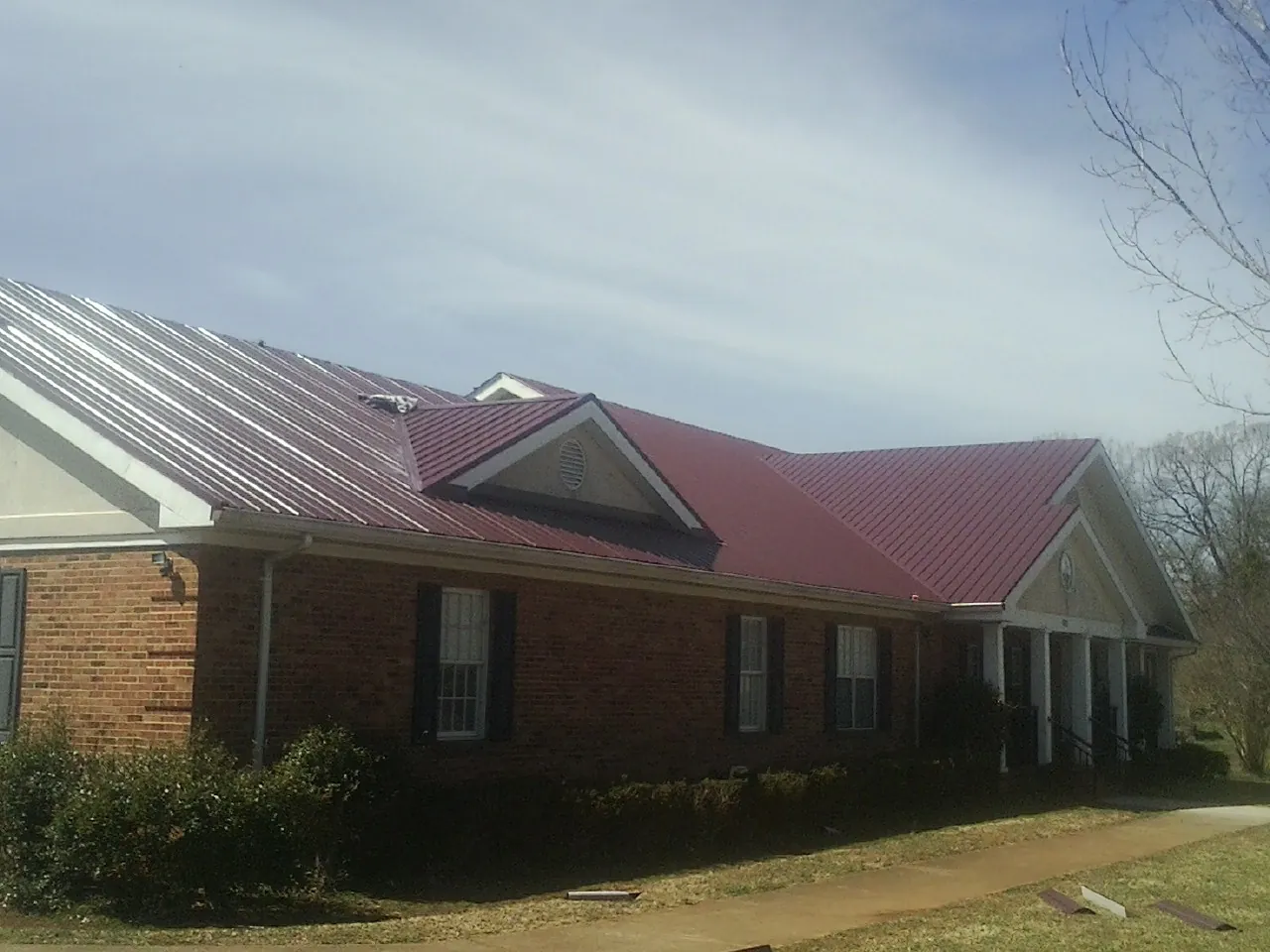 Red metal roof with gabled entries on a long brick building, from a Hail Damage Roof Repair job in Berkey