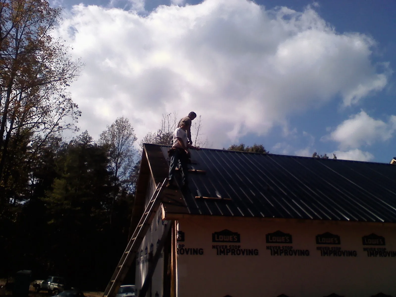 Roofer fastening dark metal panels high against a cloudy sky, from a Roof Inspection job in Berkey