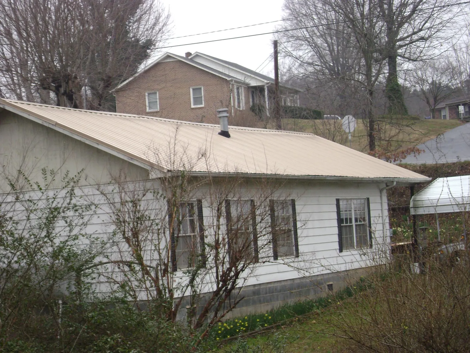 Tan metal roof on a white sided house set into a hillside — Commercial Roofing by Roofing Brothers in Berkey